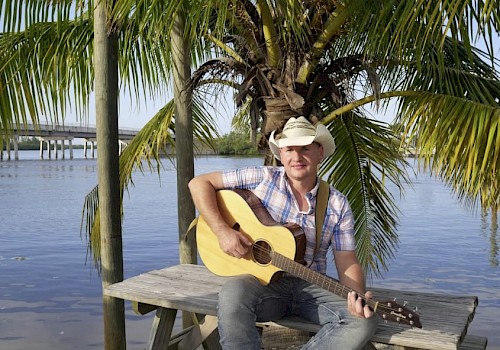 Man sitting on a picnic table with a cowboy hat and a guitar