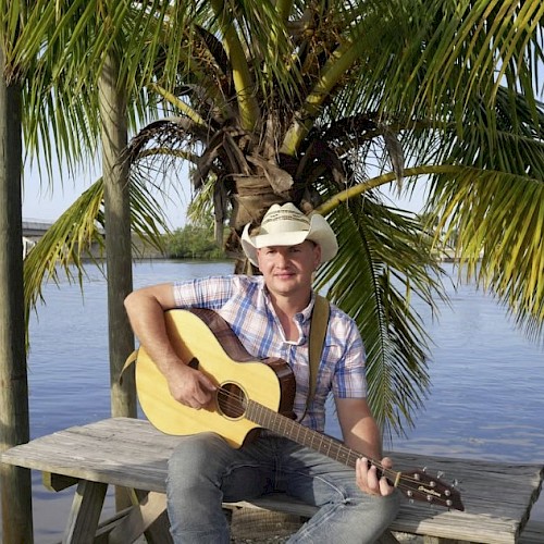 Man sitting on a picnic table with a cowboy hat and a guitar