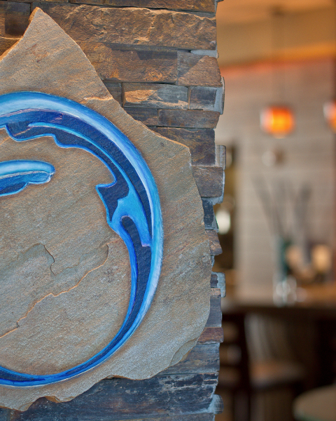 A stone plaque with a blue abstract design is mounted on a wall, in a setting with blurred lights and furnishings.