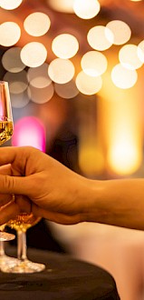 A person is preparing glasses of champagne at an elegant event with warm, festive lighting and blurred background.
