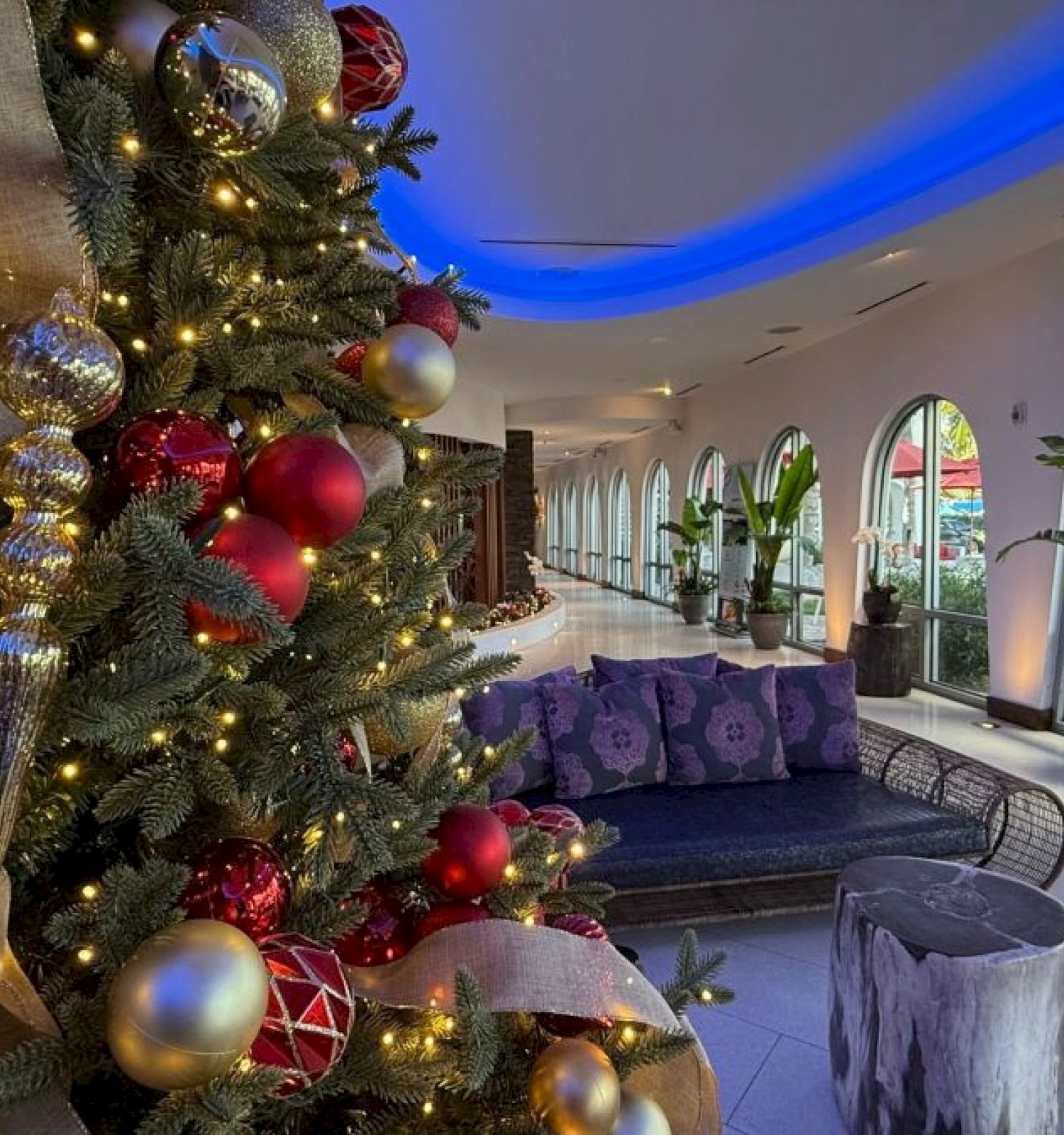 A beautifully decorated Christmas tree with red, gold, and silver ornaments and warm lights in a modern, cozy hotel lobby.