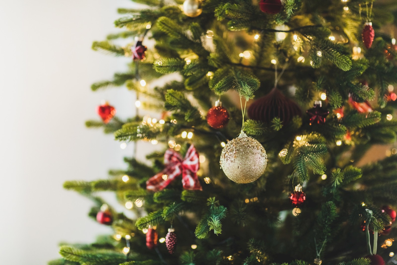 A decorated Christmas tree with lights, ornaments, and red bows. The background is light and out of focus, highlighting the tree's festive decorations.