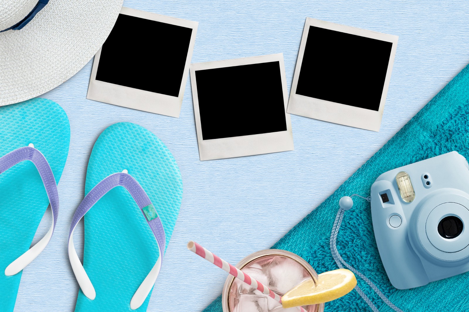 Beach essentials on a light blue surface include a wide-brimmed hat, flip-flops, a camera, a drink with a lemon slice, and some photos.