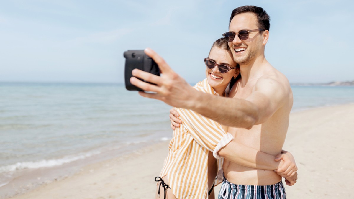 A couple is taking a selfie on the beach, smiling and enjoying sunny weather together.