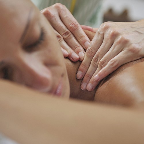 A person is receiving a back massage, lying face down, with hands applying pressure on their back for relaxation and therapy.