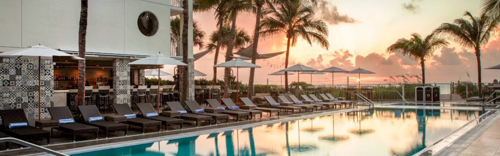 A serene poolside scene at sunset with palm trees, lounge chairs, and a bar area, creating a tropical vacation vibe.