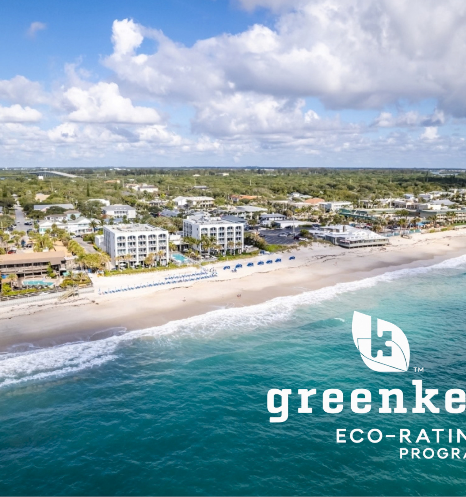 Aerial view of a beachside town with hotels, palm trees, and blue umbrellas, promoting Green Key's eco-rating program for sustainability.