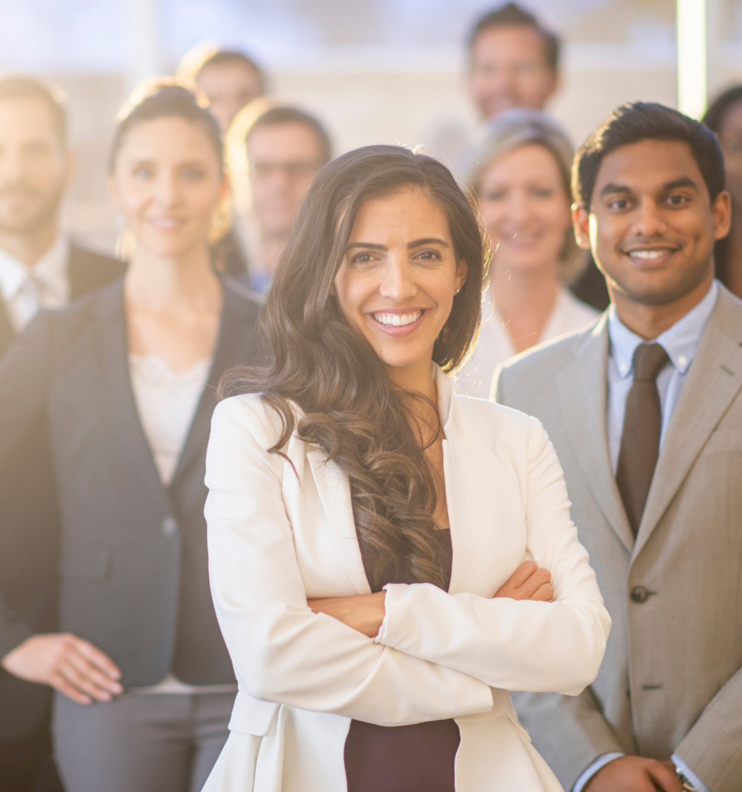 A diverse group of professionally dressed people is smiling at the camera, with a woman and a man in business attire standing prominently in the front.