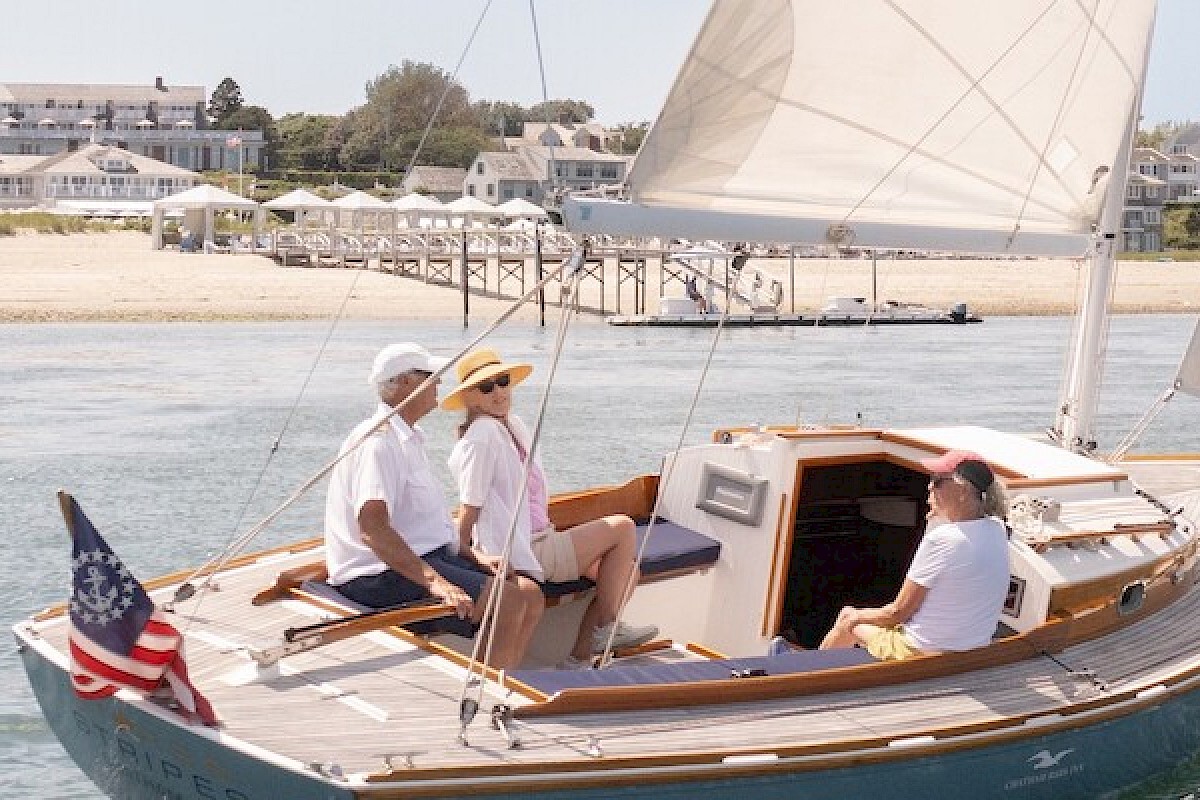 A group of four people enjoying a sailboat ride on a sunny day near a coastal town.