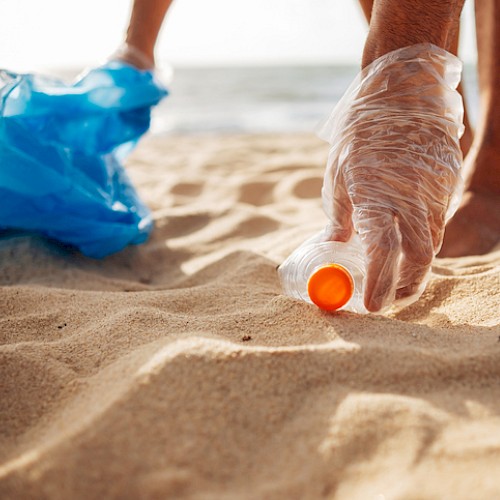 Someone is picking up litter, specifically a plastic bottle, from the beach to help keep it clean and protect the environment.