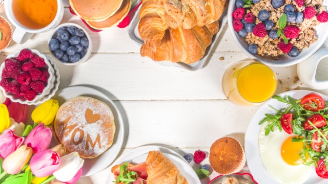 A breakfast spread with croissants, eggs, berries, muffins, honey, flowers, and beverages on a white table.