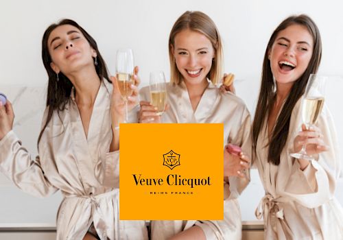 Three women in robes are holding champagne glasses, appearing to celebrate. The Veuve Clicquot logo is superimposed in the center.
