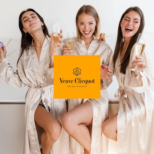 Three women in robes are holding champagne glasses, appearing to celebrate. The Veuve Clicquot logo is superimposed in the center.