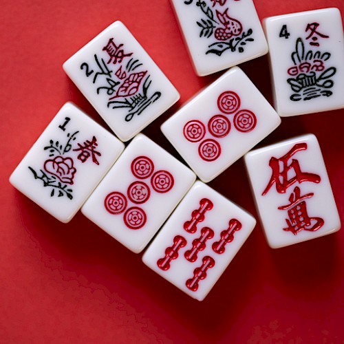 The image shows a set of Mahjong tiles arranged on a red surface, featuring various traditional Chinese characters and symbols.