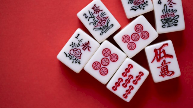 The image shows a set of Mahjong tiles arranged on a red surface, featuring various traditional Chinese characters and symbols.