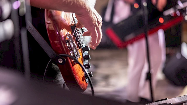A musician is playing an electric guitar during a live performance, with focus on their hand strumming the instrument.