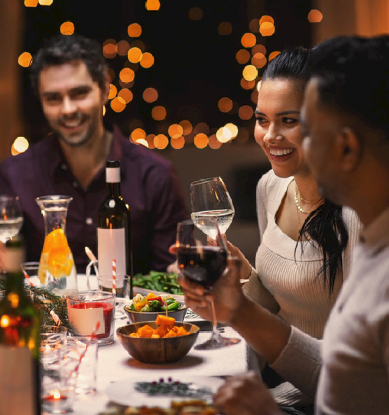 A group enjoys a festive dinner with drinks and food in a warmly lit setting, sharing a joyful moment together.