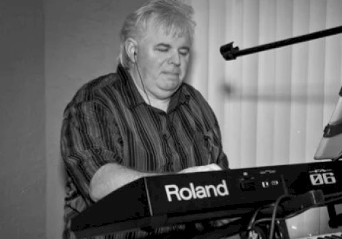 A person is playing a Roland keyboard, using a stand with a mounted device and a microphone.