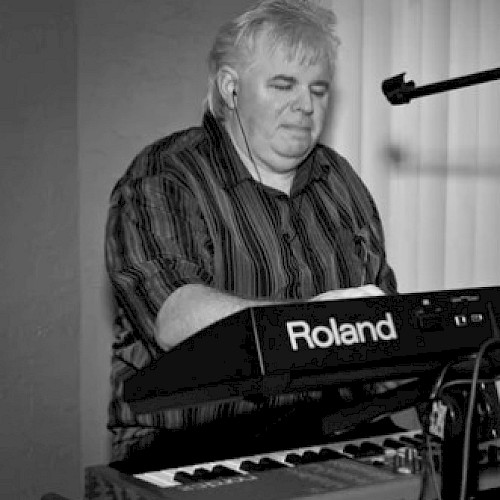 A person is playing a Roland keyboard, using a stand with a mounted device and a microphone.