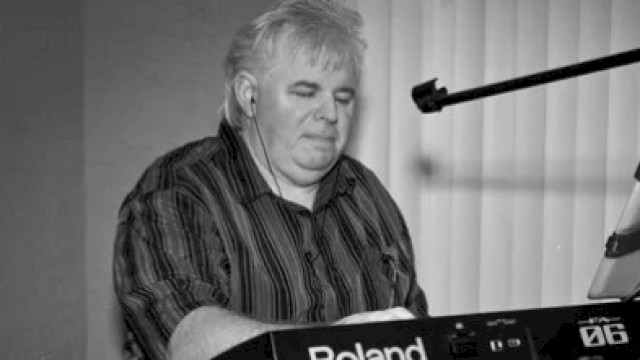 A person is playing a Roland keyboard, using a stand with a mounted device and a microphone.