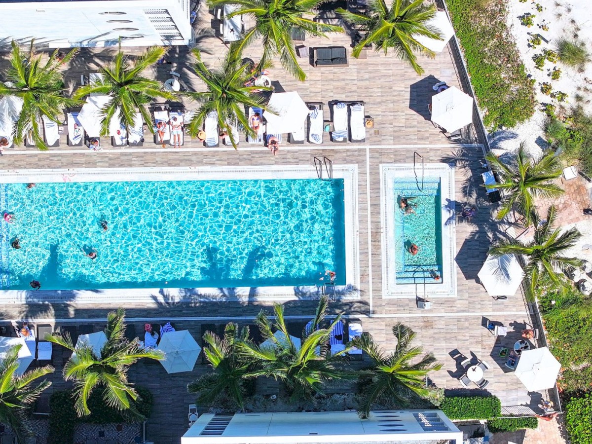 Aerial view of a pool area with sun loungers and palm trees.