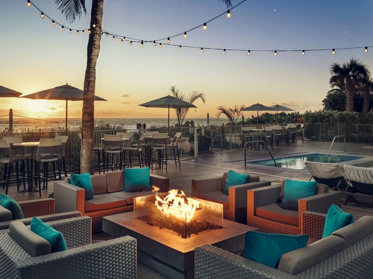 Outdoor lounge with firepit, seating, poolside ambiance, and a sunset view.