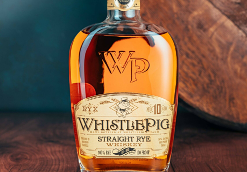 A bottle of WhistlePig 10-Year Straight Rye Whiskey is on a wooden surface, with its label prominently showing.
