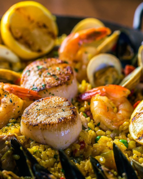 A seafood paella with scallops, shrimp, mussels, clams, and lemons on a bed of saffron rice, garnished with parsley.