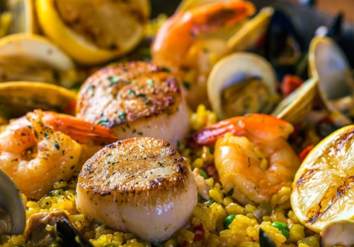 A seafood paella with scallops, shrimp, mussels, clams, and lemons on a bed of saffron rice, garnished with parsley.