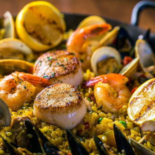 A seafood paella with scallops, shrimp, mussels, clams, and lemons on a bed of saffron rice, garnished with parsley.