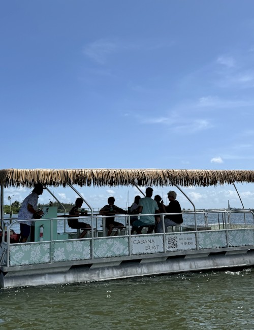 A group of people on a boat with a thatched roof, cruising on a body of water under a clear blue sky.