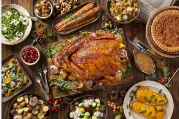 A Thanksgiving feast with roasted turkey, assorted vegetables, gravy, pie, cranberries, and various side dishes on a wooden table.