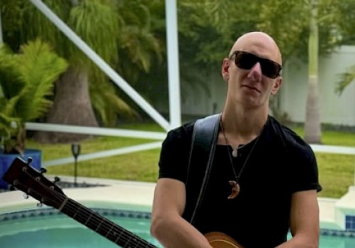Marco George posing with his guitar in front of a pool