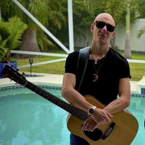 Marco George posing with his guitar in front of a pool