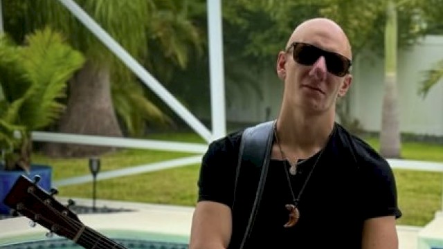 Marco George posing with his guitar in front of a pool