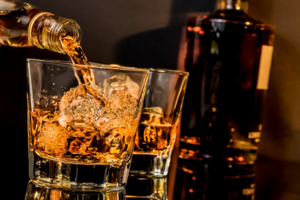 A bottle pours amber liquid into two glasses with ice cubes, set against a dark background.