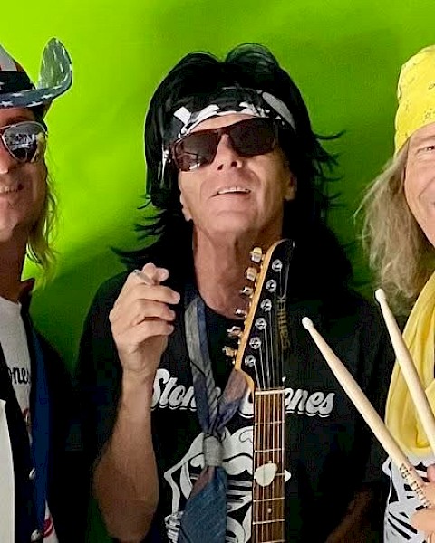 Three people are dressed in rock-themed outfits, holding instruments, and smiling in front of a green background.