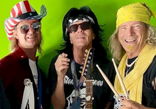 Three people are dressed in rock-themed outfits, holding instruments, and smiling in front of a green background.