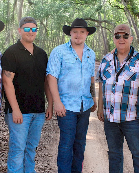 Five people standing on a woodland path, wearing hats and casual clothes, smiling at the camera.