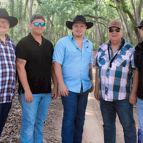 Five people standing on a woodland path, wearing hats and casual clothes, smiling at the camera.