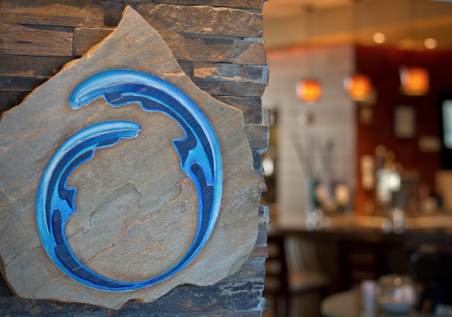 A wall-mounted stone plaque featuring a blue, wave-like design, with a blurred bar area in the background ending the sentence.