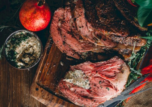 The image shows a sliced Prime Rib on a wooden board with herbs, a knife, orange slices, a pomegranate, and a bowl of seasoning.