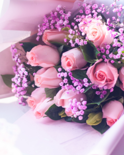 A bouquet of pink roses mixed with small purple flowers, wrapped in light paper, creating an elegant and charming floral arrangement.