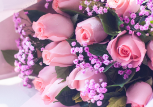 A bouquet of pink roses mixed with small purple flowers, wrapped in light paper, creating an elegant and charming floral arrangement.