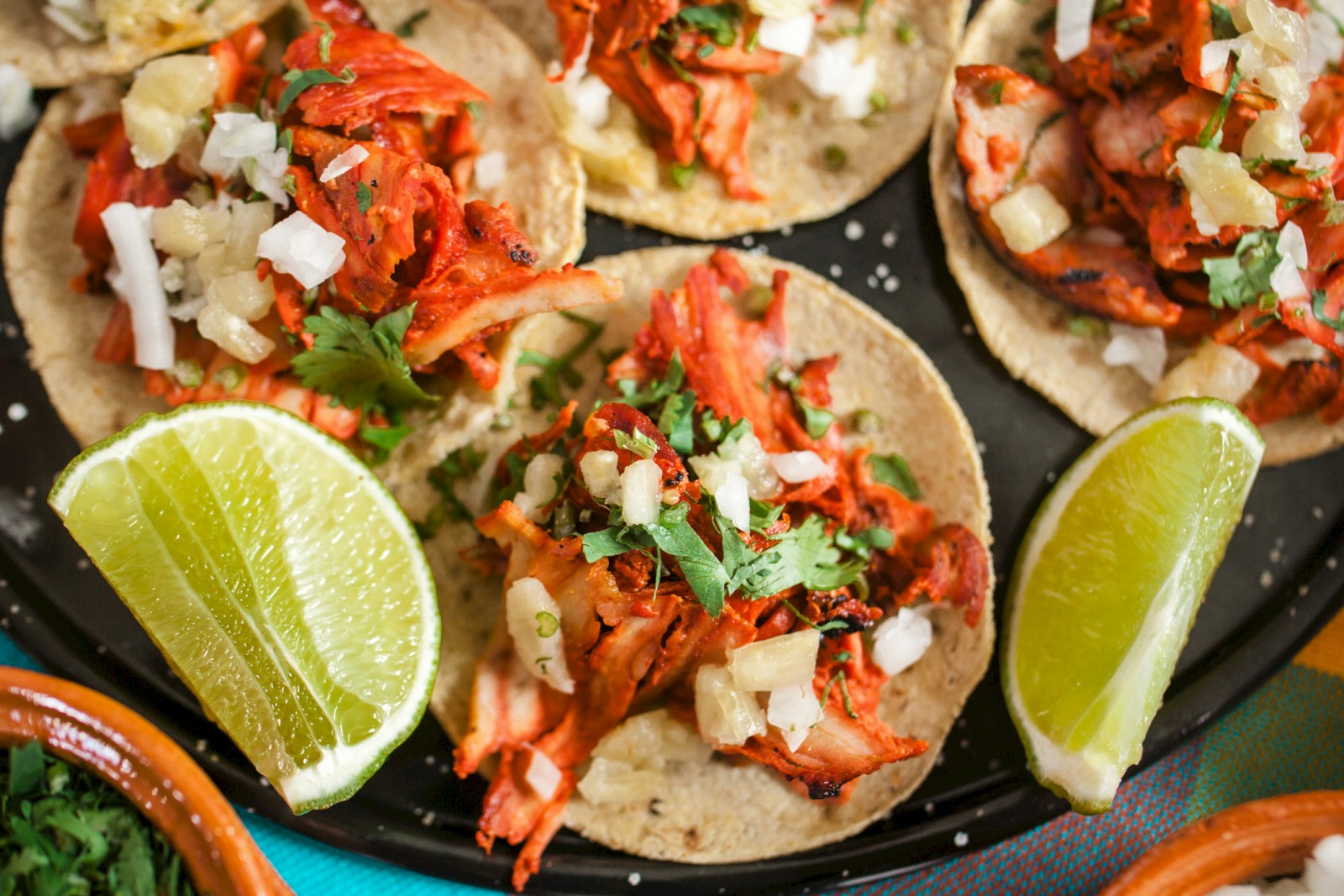 Tacos with meat, onions, cilantro, and lime wedges on the side are shown on a plate.