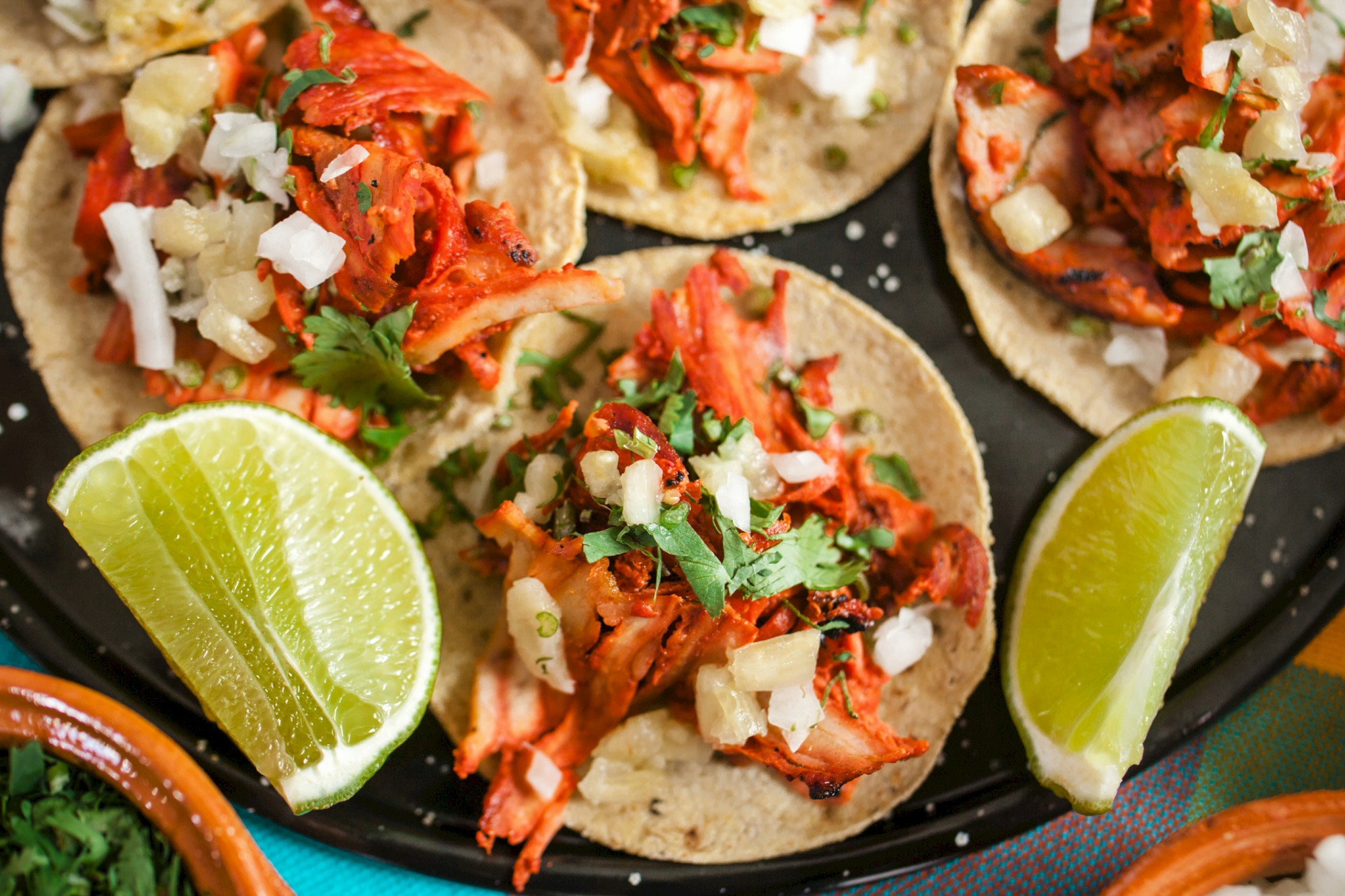 Tacos with meat, onions, cilantro, and lime wedges on the side are shown on a plate.