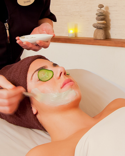 A person is receiving a facial treatment with a mask applied; they have a cucumber slice on their eye.
