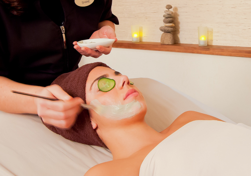 A person is receiving a facial treatment with a mask applied; they have a cucumber slice on their eye.