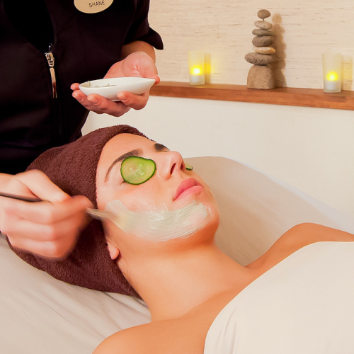A person is receiving a facial treatment with a mask applied; they have a cucumber slice on their eye.
