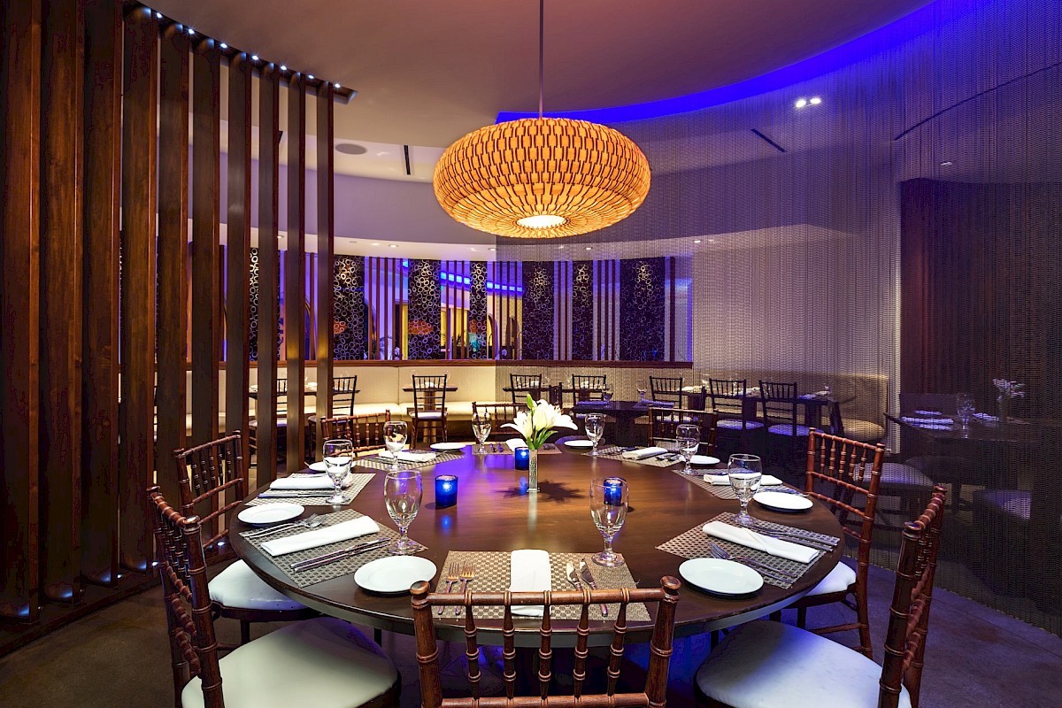 A round dining table set with plates and glasses in an elegant restaurant featuring wooden elements and ambient lighting.